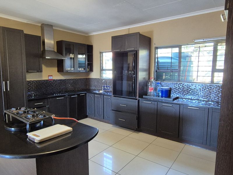 A functional kitchen featuring dark wood cabinetry, granite countertops, a mosaic tile backsplash, and tiled flooring with integrated storage and an extractor fan.