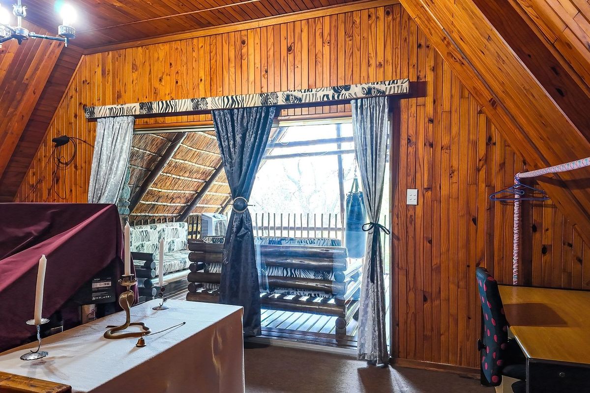 A bedroom featuring extensive timber wall paneling, a sloped ceiling, and sliding glass doors that open onto a balcony.