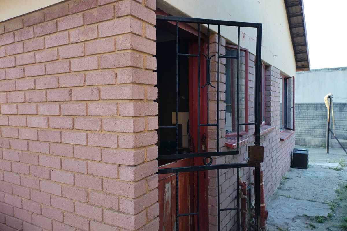 Rear exterior view of the property featuring brick wall construction, a security gate, and concrete paving.