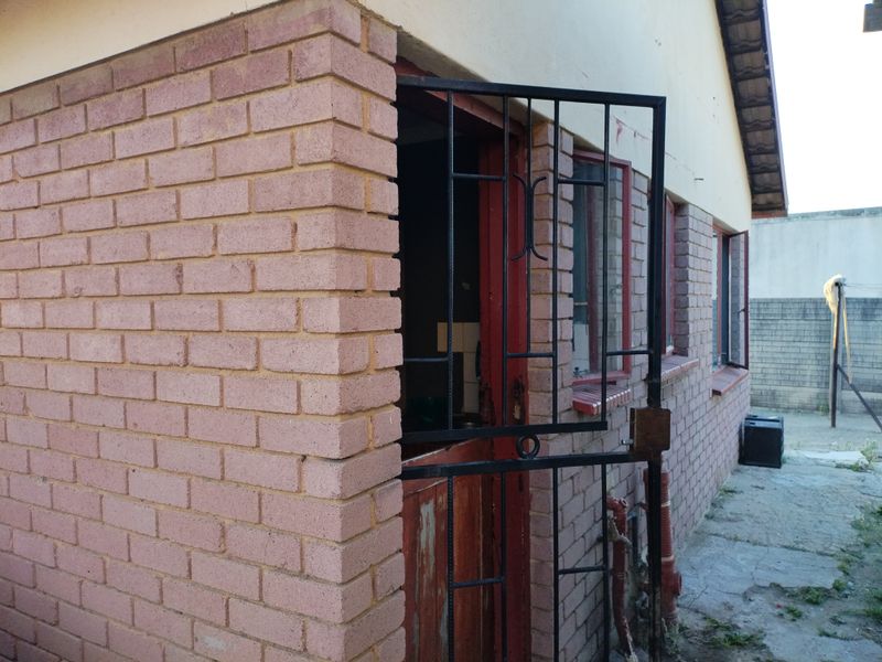 Rear exterior view of the property featuring brick wall construction, a security gate, and concrete paving.