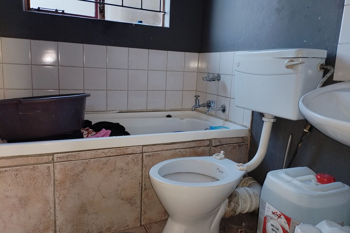 A dated bathroom featuring a standard bathtub, toilet, and washbasin with visible plumbing and worn wall finishes, requiring cosmetic updates and maintenance.