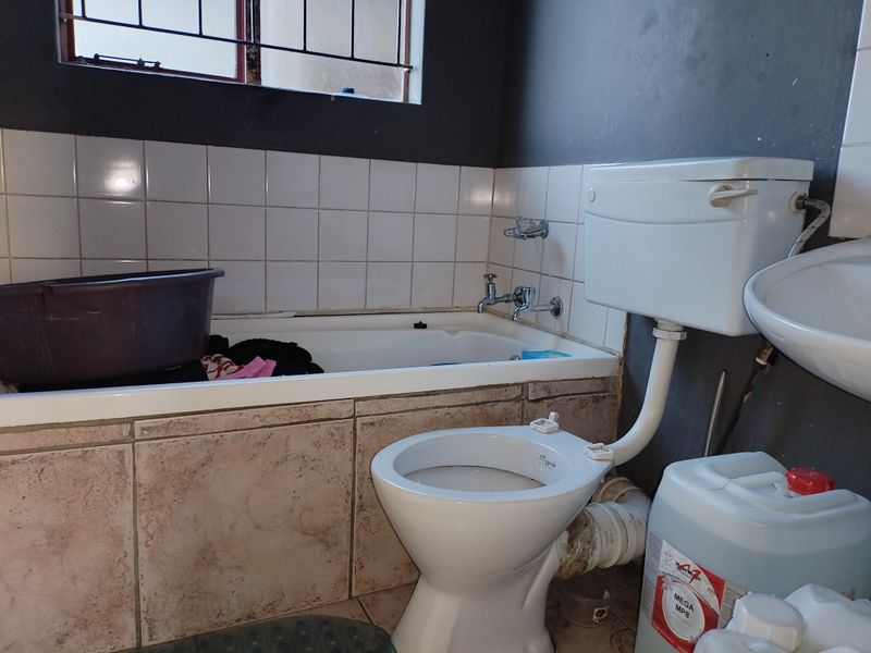 A dated bathroom featuring a standard bathtub, toilet, and washbasin with visible plumbing and worn wall finishes, requiring cosmetic updates and maintenance.