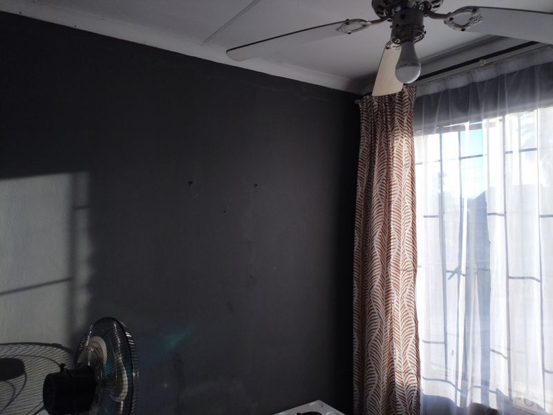 A bedroom featuring a ceiling fan, security bars on the window, and dark-painted walls.