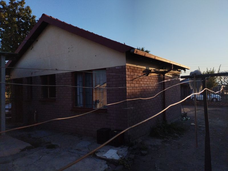 Rear view of a brick house featuring a tiled roof, metal window frames with security bars, and visible wear to the eaves and guttering.