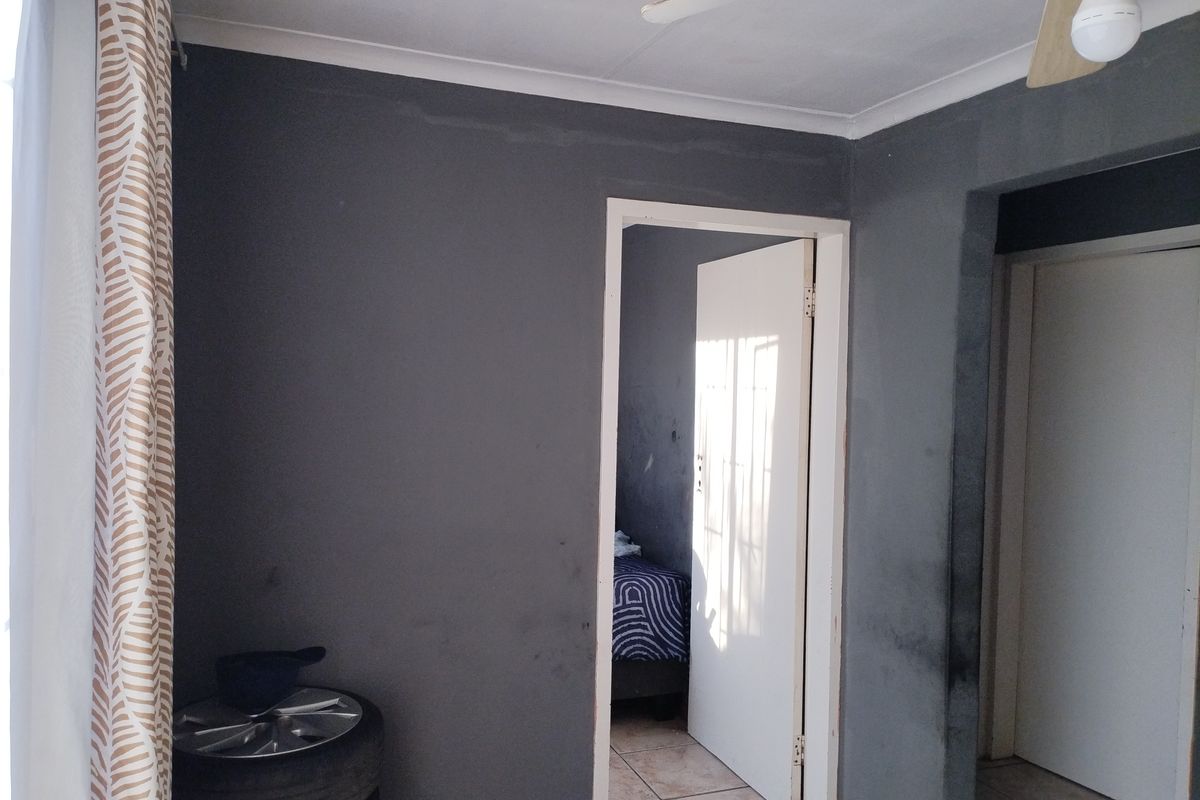 A bedroom interior featuring dark grey painted walls, tiled flooring, and a ceiling fan, requiring cosmetic updates to improve the overall finish.