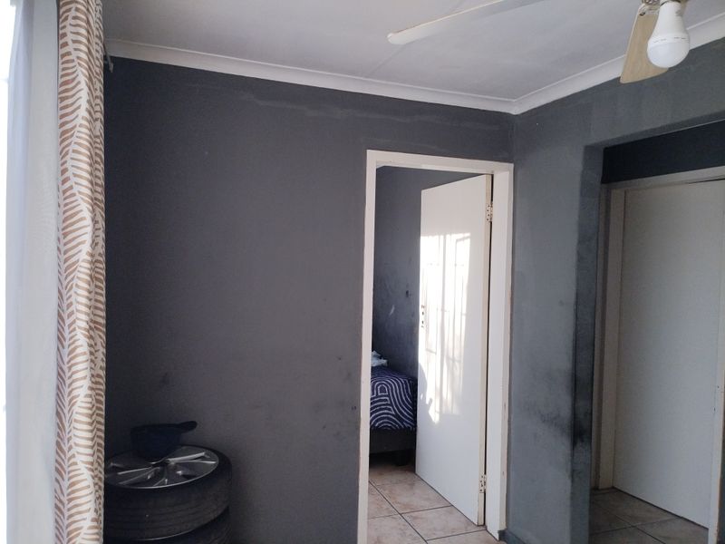 A bedroom interior featuring dark grey painted walls, tiled flooring, and a ceiling fan, requiring cosmetic updates to improve the overall finish.