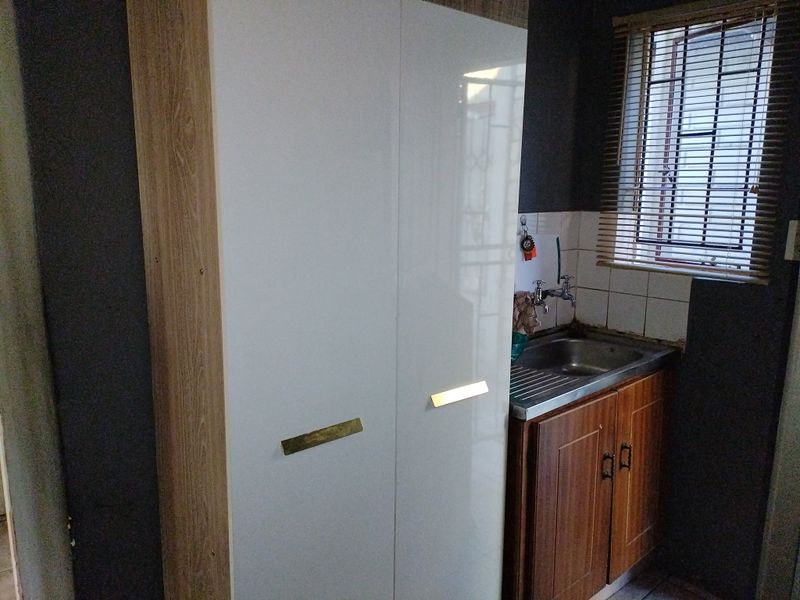 A functional scullery area featuring a stainless steel sink, tiled splashback, and built-in cabinetry with a window providing natural light.