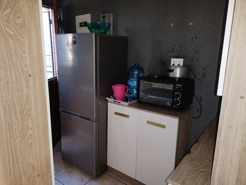 A compact scullery or utility area featuring base cabinetry, tiled flooring, and an electrical distribution board, requiring cosmetic wall repairs.