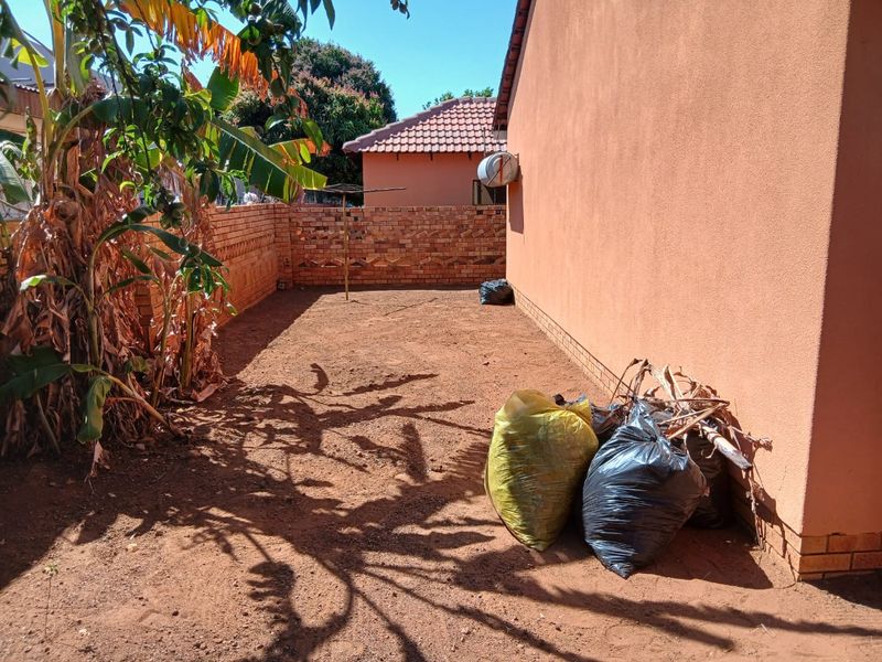 A rear exterior area featuring a brick boundary wall and a rotary clothesline, currently requiring landscaping and general maintenance.