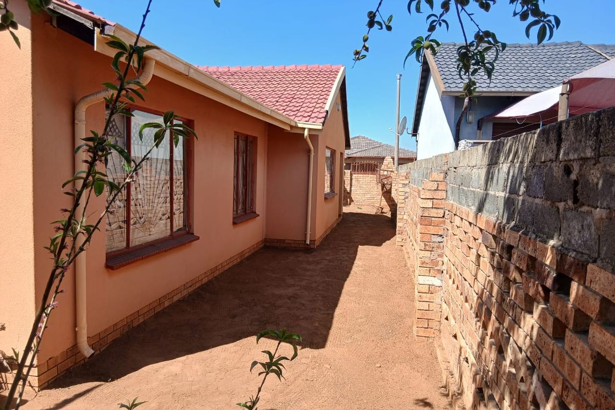Side exterior view of the house featuring a tiled roof, painted exterior walls, and a brick boundary wall with an unfinished ground area.
