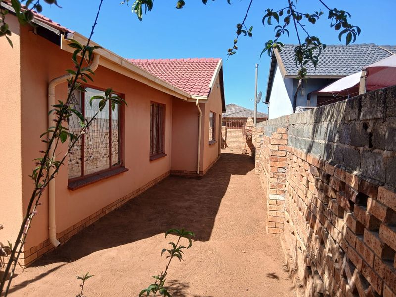 Side exterior view of the house featuring a tiled roof, painted exterior walls, and a brick boundary wall with an unfinished ground area.