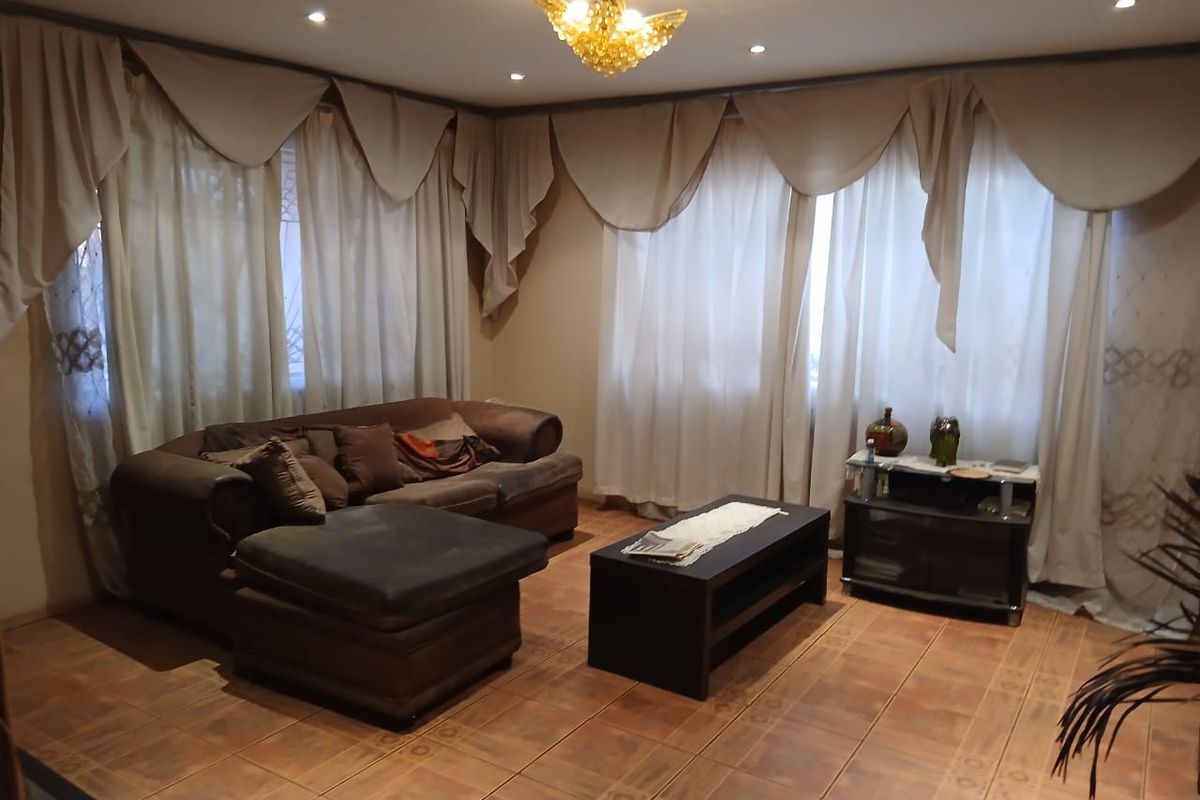 A living room featuring tiled flooring, recessed downlighting, and a decorative central chandelier, offering a functional space with neutral wall tones.