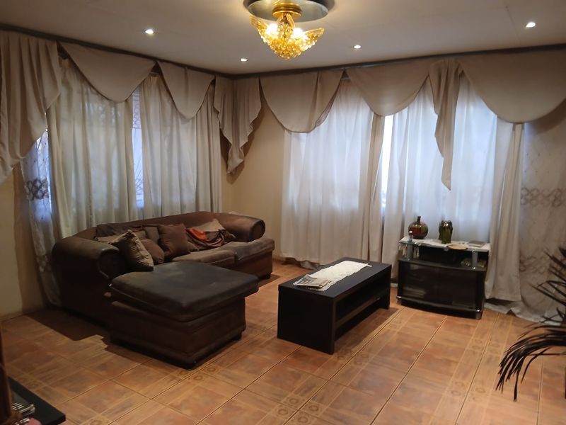 A living room featuring tiled flooring, recessed downlighting, and a decorative central chandelier, offering a functional space with neutral wall tones.