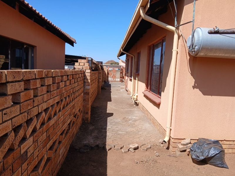 Side passage of the property featuring a brick boundary wall, paved walkway, and external geyser unit.