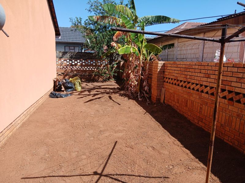 A rear yard area featuring a brick boundary wall with decorative detailing and razor wire, currently with an unlandscaped earth surface.