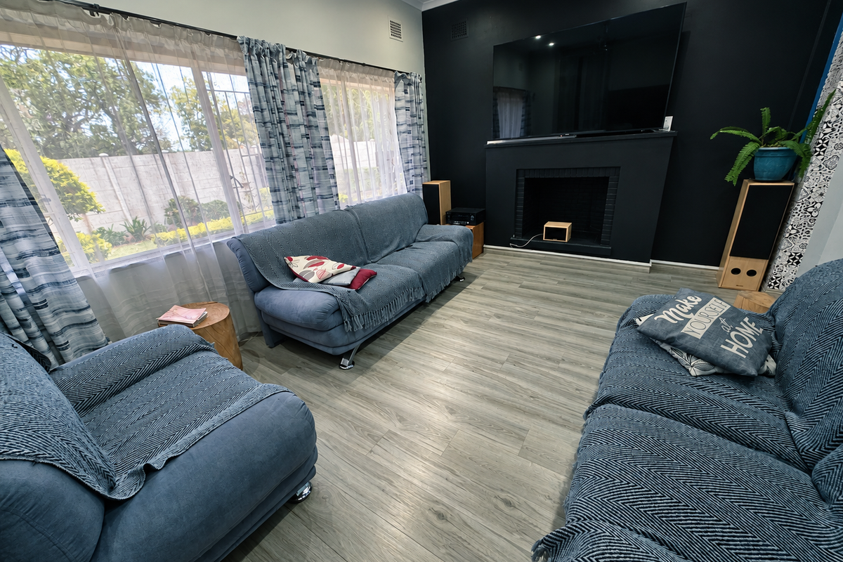 A well-maintained living room featuring modern laminate flooring, a striking black feature wall with a built-in fireplace, and large windows allowing ample natural light.