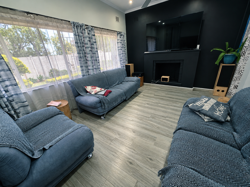 A well-maintained living room featuring modern laminate flooring, a striking black feature wall with a built-in fireplace, and large windows allowing ample natural light.
