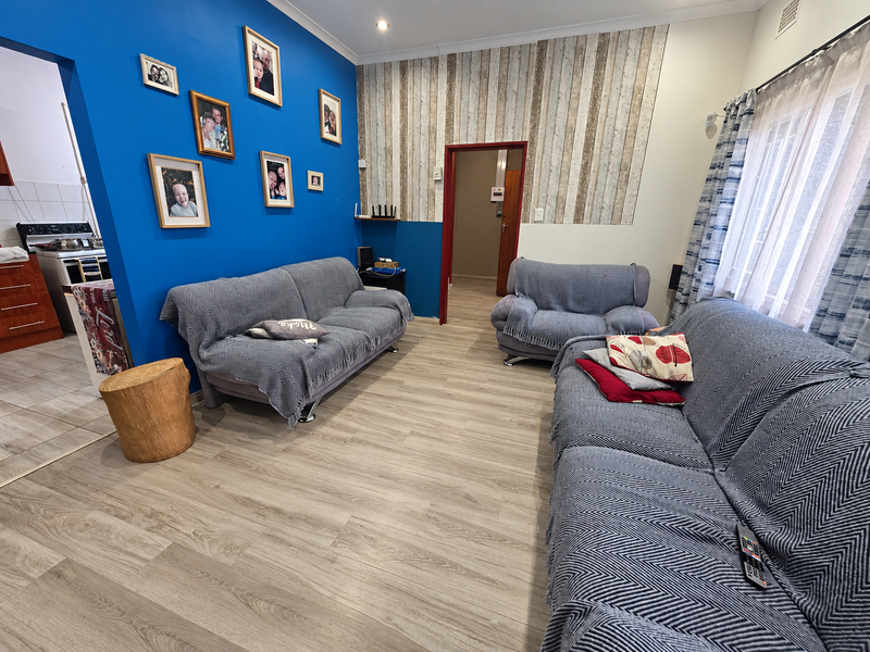 A living room featuring laminate flooring, a bold blue accent wall, and a timber-look feature wall, with an adjacent view into the kitchen area.