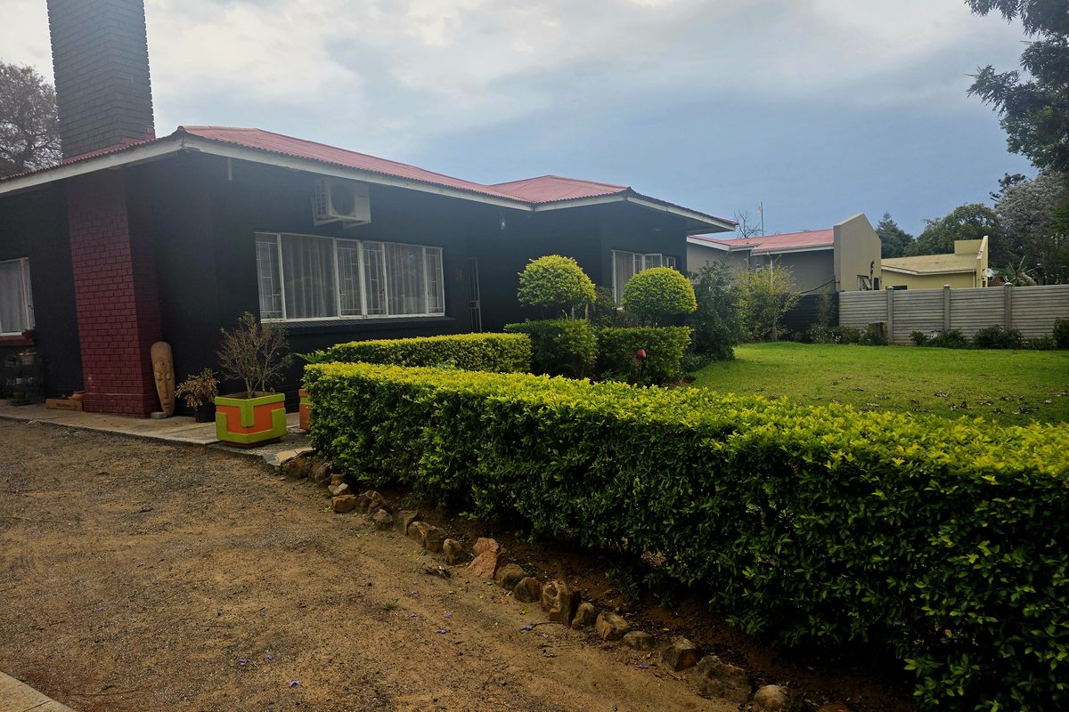 Rear view of the house featuring a dark exterior finish, brick chimney, metal roof, and a well-maintained garden with established hedges.