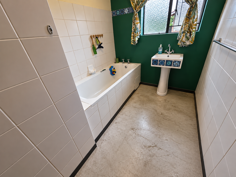 A functional bathroom featuring a pedestal washbasin, a built-in bathtub, and tiled wall finishes, offering a clean space ready for potential cosmetic updates.