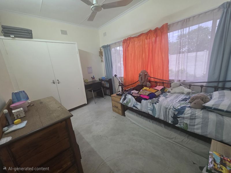 A functional bedroom featuring a built-in wardrobe, ceiling fan, and large window providing natural light.