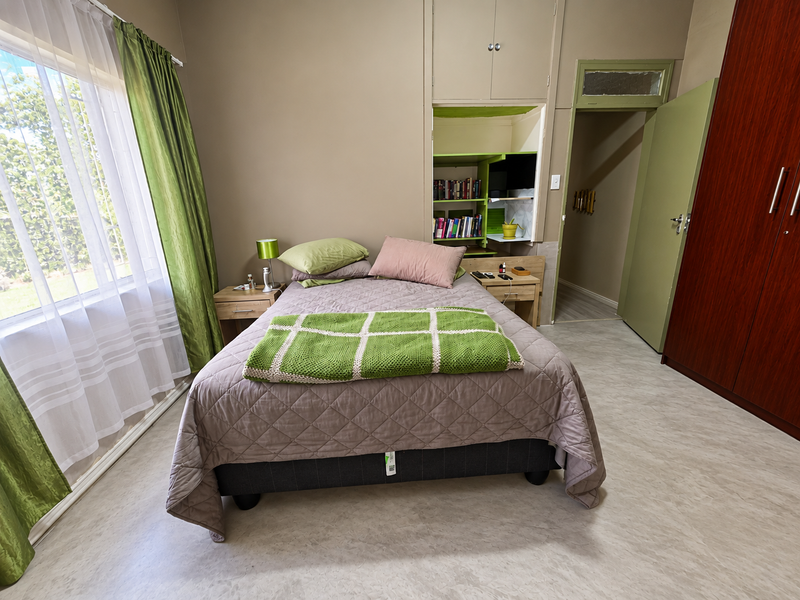 A bedroom featuring built-in cupboards, recessed shelving, and vinyl flooring, with natural light provided by a large window.