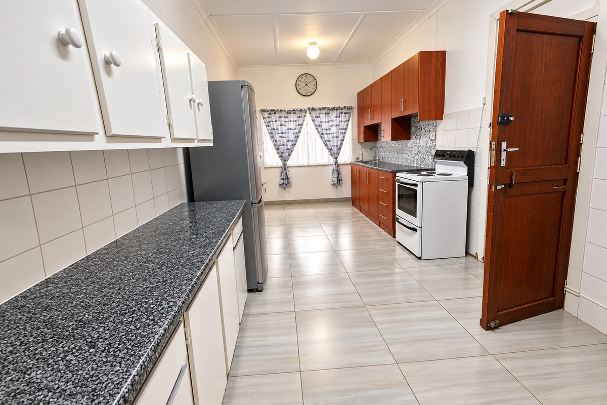A functional kitchen featuring laminate countertops, built-in cabinetry, a tiled backsplash, and a freestanding stove, with neutral tiled flooring throughout.