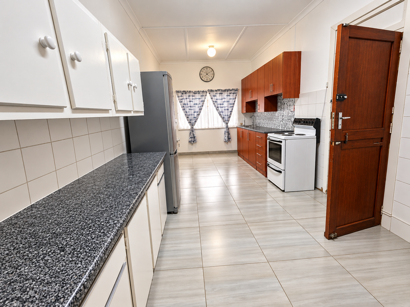A functional kitchen featuring laminate countertops, built-in cabinetry, a tiled backsplash, and a freestanding stove, with neutral tiled flooring throughout.