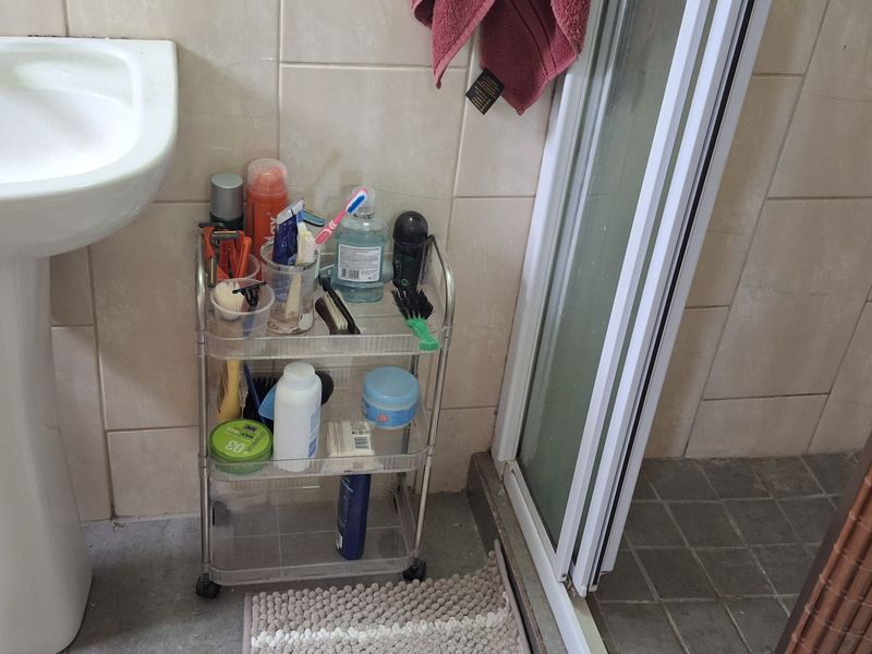 A compact bathroom featuring a pedestal washbasin and a shower enclosure with tiled wall and floor finishes.