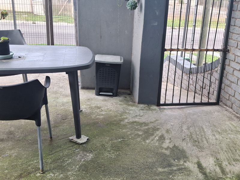 Covered patio area featuring exposed brickwork, concrete flooring, and a metal security gate, providing a functional outdoor space.