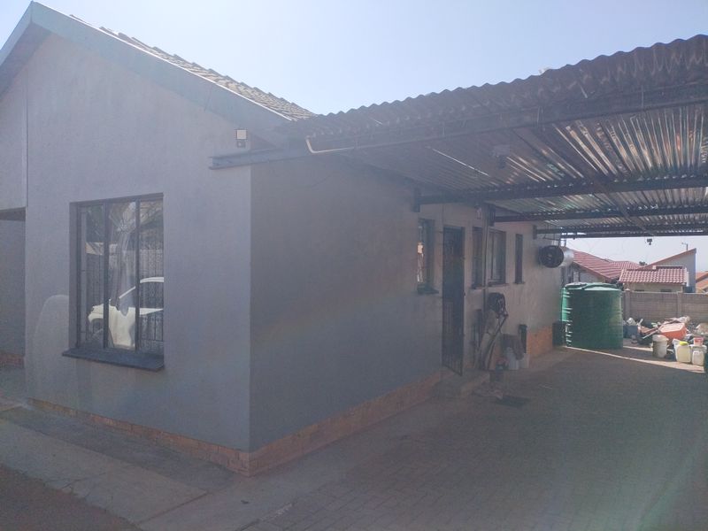 Front exterior view of the house featuring a paved driveway, a corrugated metal carport, and a water storage tank.