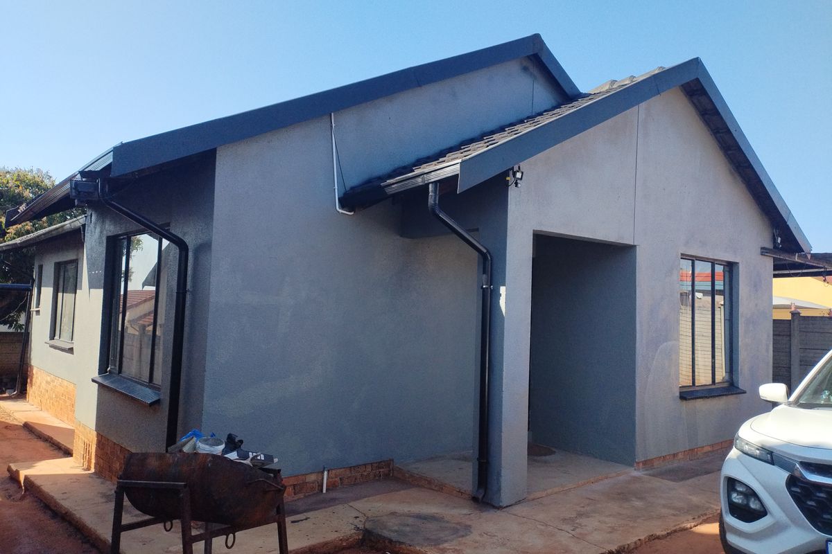 Rear view of a modern grey-painted house featuring a tiled roof, black gutters, and a concrete apron surrounding the structure.