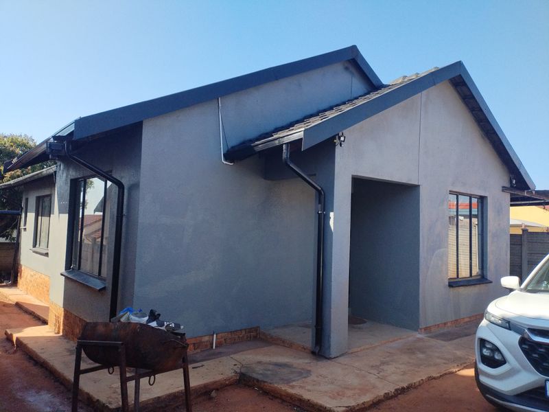 Rear view of a modern grey-painted house featuring a tiled roof, black gutters, and a concrete apron surrounding the structure.
