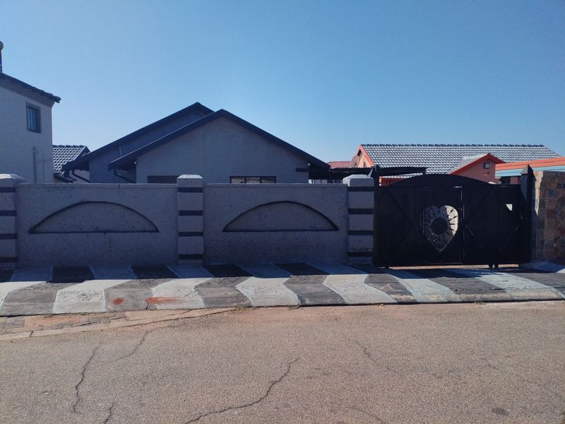 Front view of the property featuring a perimeter wall with decorative concrete pillars and a black metal driveway gate.