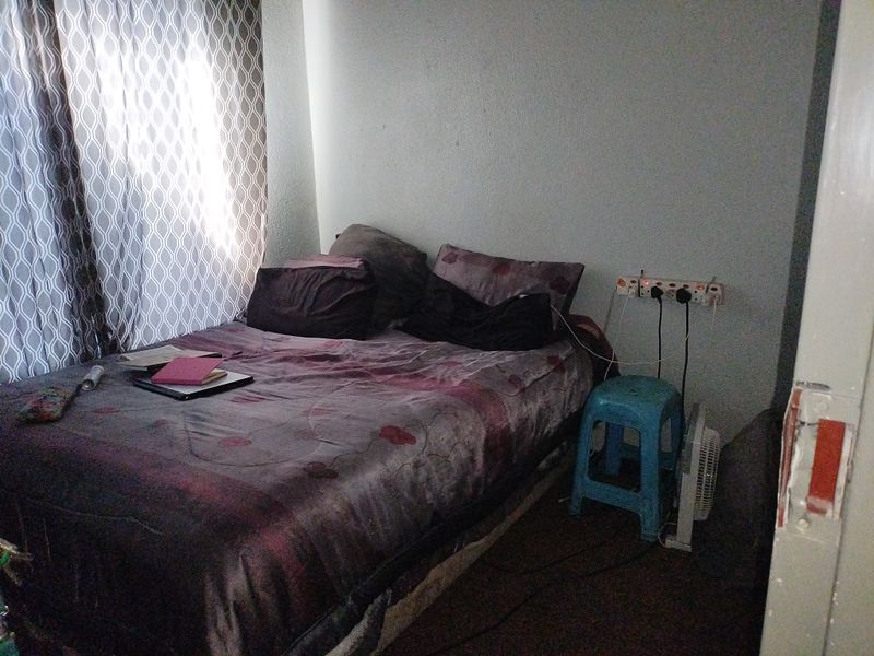 A compact bedroom featuring window curtains and visible wear on the door frame, requiring minor maintenance and cosmetic updates.
