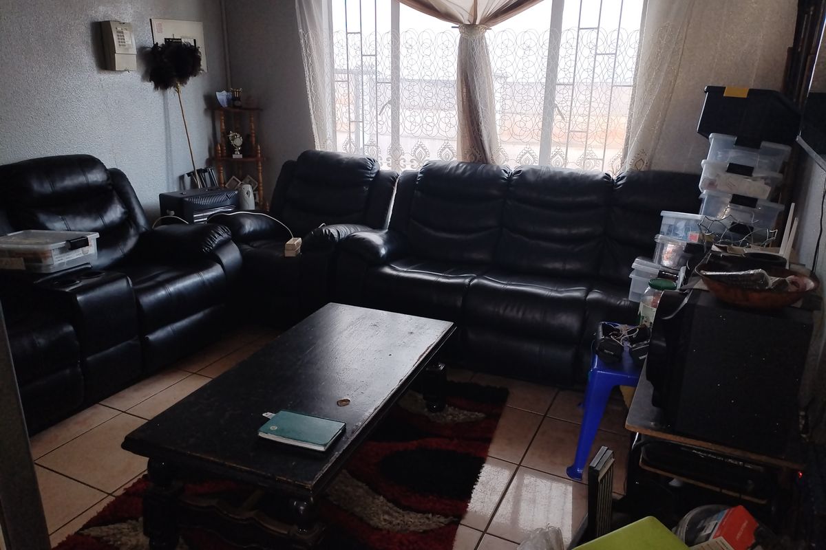 A living room featuring tiled flooring and a large window fitted with security bars, providing natural light to the space.