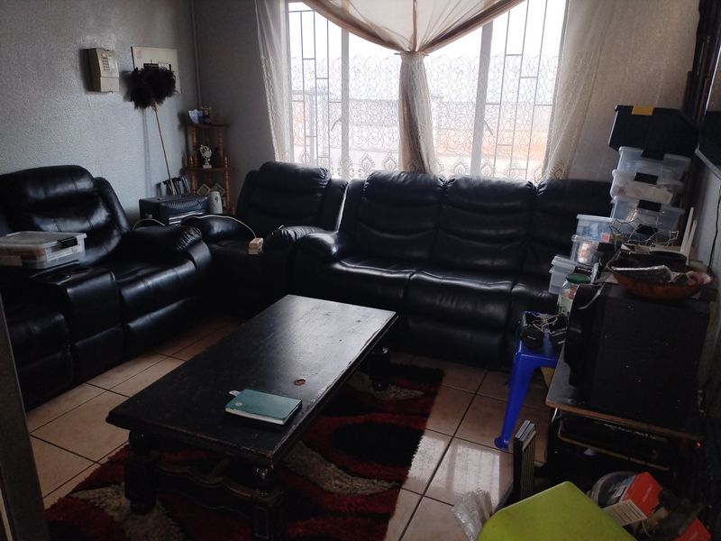 A living room featuring tiled flooring and a large window fitted with security bars, providing natural light to the space.