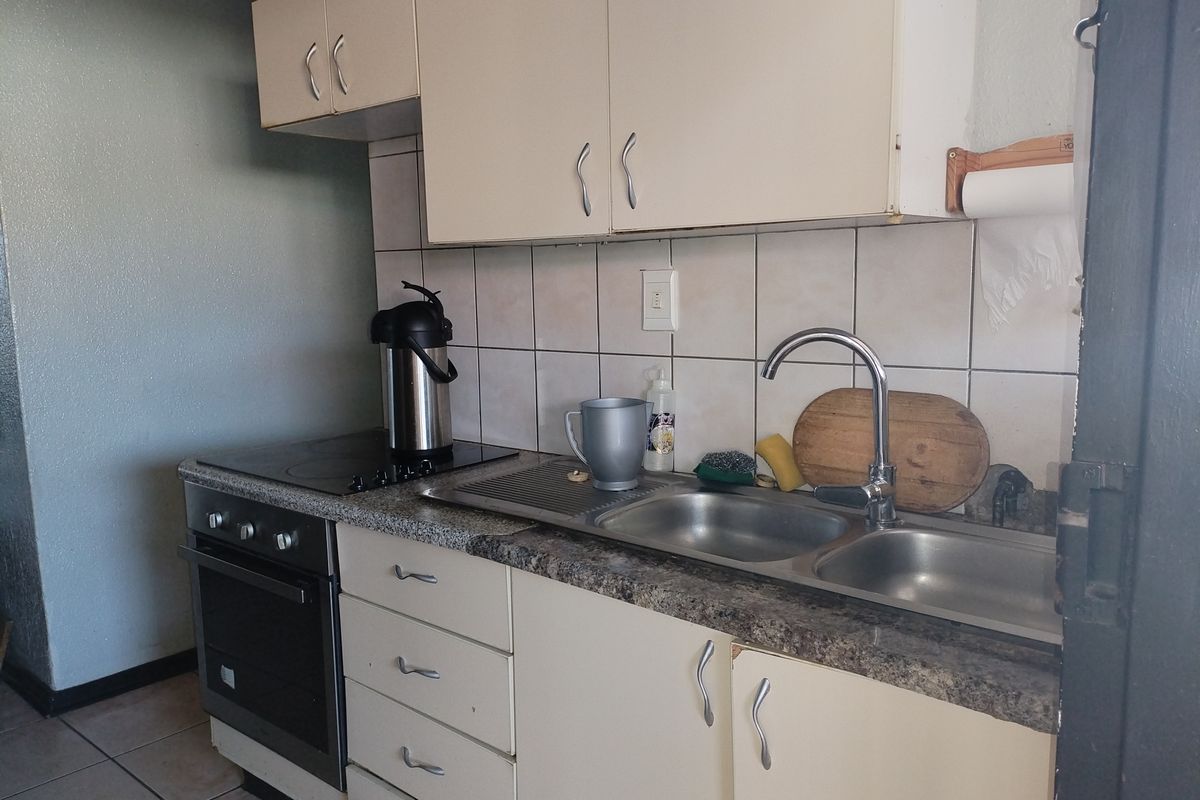 A compact kitchen featuring built-in cabinetry, a double bowl stainless steel sink, and an integrated oven with an electric hob.