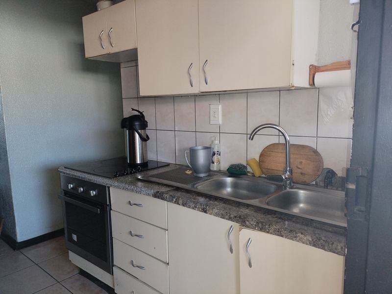 A compact kitchen featuring built-in cabinetry, a double bowl stainless steel sink, and an integrated oven with an electric hob.
