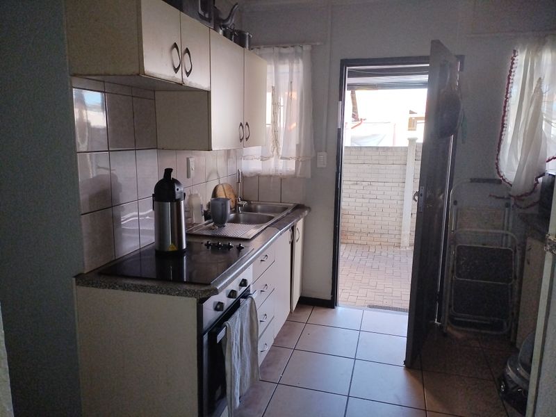A functional kitchen featuring built-in cabinetry, an electric hob, oven, and tiled flooring, with direct access to an outdoor paved area.