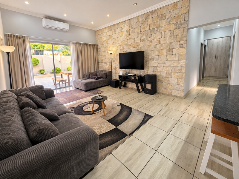 Spacious living room featuring a textured stone accent wall, tiled flooring, and large sliding glass doors providing seamless access to the outdoor patio area.
