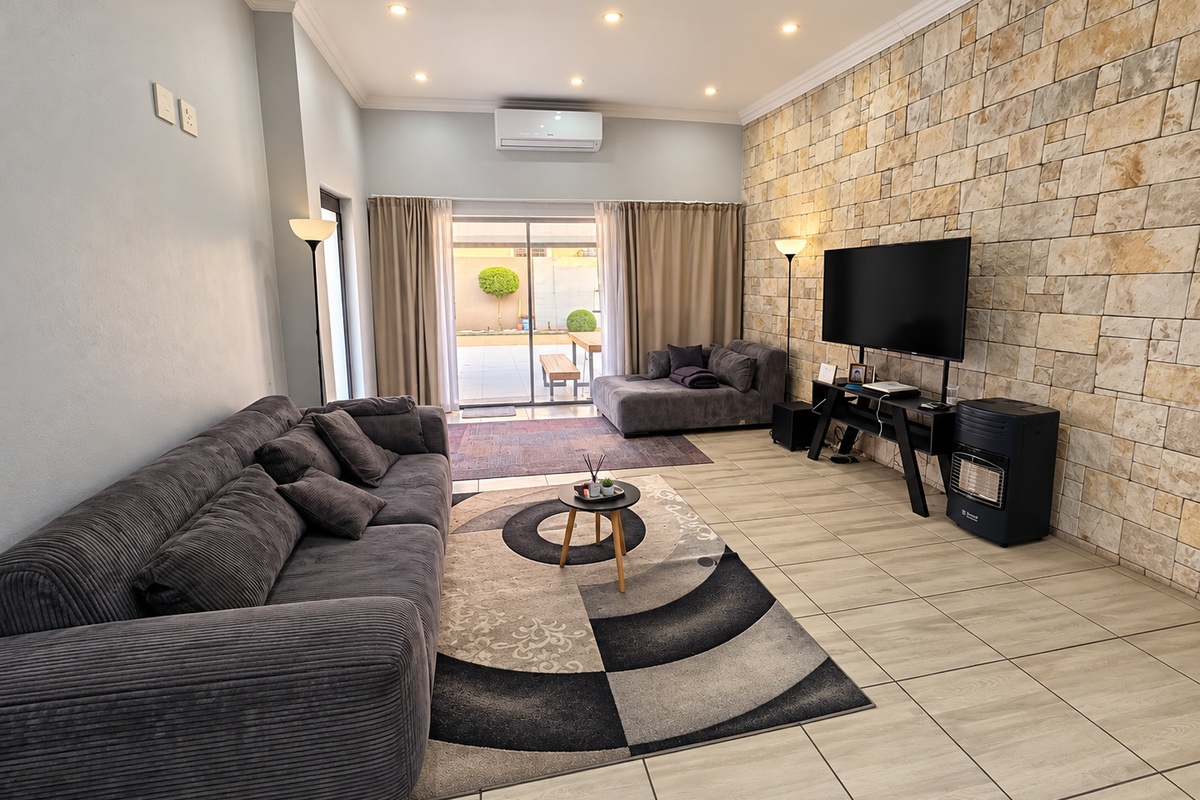 Spacious living room featuring a textured stone feature wall, tiled flooring, recessed lighting, and direct access to the outdoor patio area.