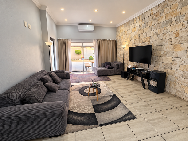 Spacious living room featuring a textured stone feature wall, tiled flooring, recessed lighting, and direct access to the outdoor patio area.