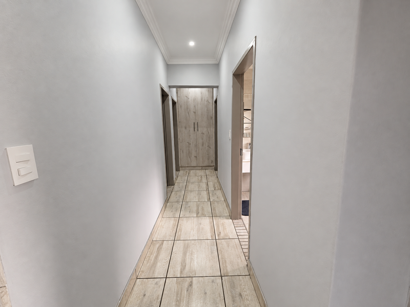 A clean, well-lit hallway featuring modern wood-look floor tiles, built-in storage cupboards, and recessed ceiling lighting.