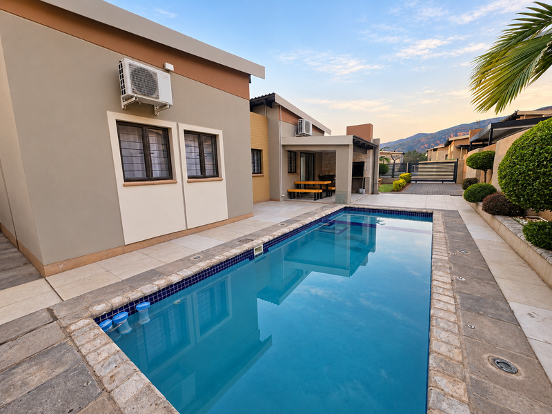 A well-maintained outdoor area featuring a rectangular swimming pool, paved surround, and a covered patio space with integrated air conditioning units.