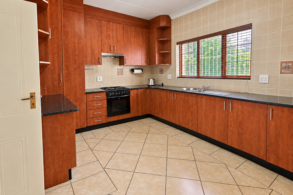 A functional kitchen featuring warm-toned wooden cabinetry, granite countertops, a built-in oven with gas hob, and tiled flooring throughout.