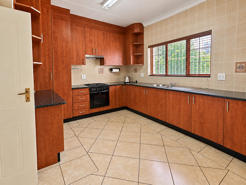 A functional kitchen featuring warm-toned wooden cabinetry, granite countertops, a built-in oven with gas hob, and tiled flooring throughout.