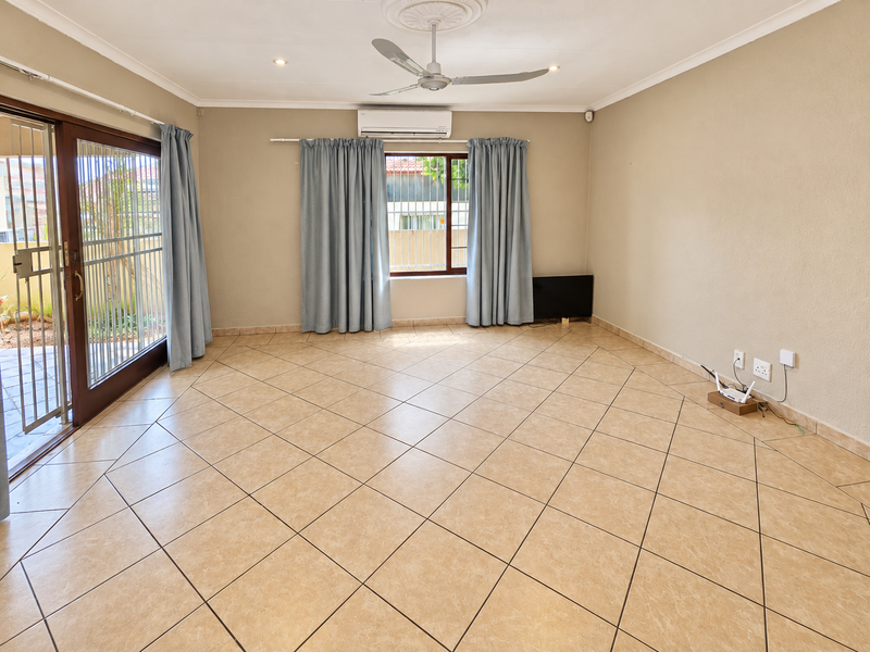 Spacious living room featuring neutral tiled flooring, a ceiling fan, split-system air conditioning, and direct access to the outdoor area via a sliding glass door.