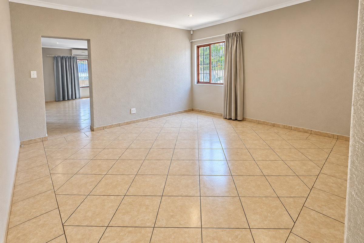 A spacious, empty living room featuring neutral tiled flooring, recessed downlighting, and a window with security bars, offering a clean and versatile living space.