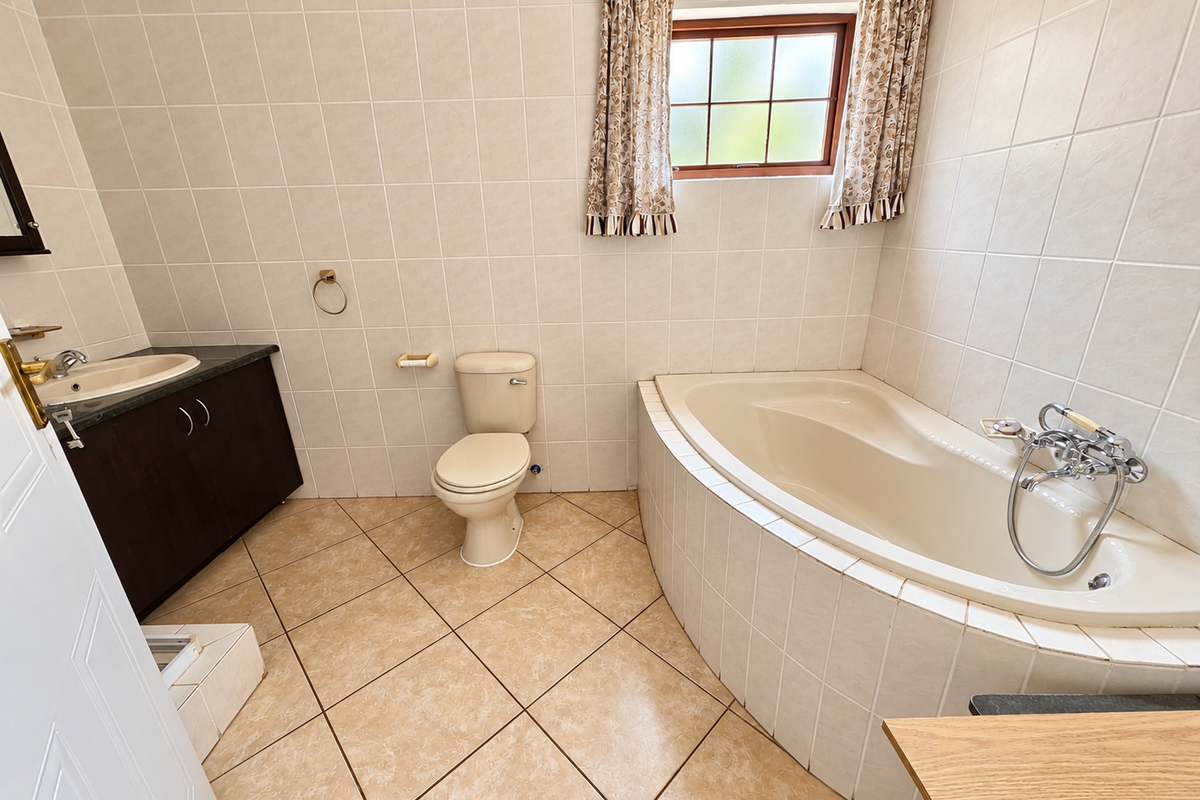 A functional bathroom featuring a corner bathtub, built-in vanity with basin, toilet, and neutral wall and floor tiling.
